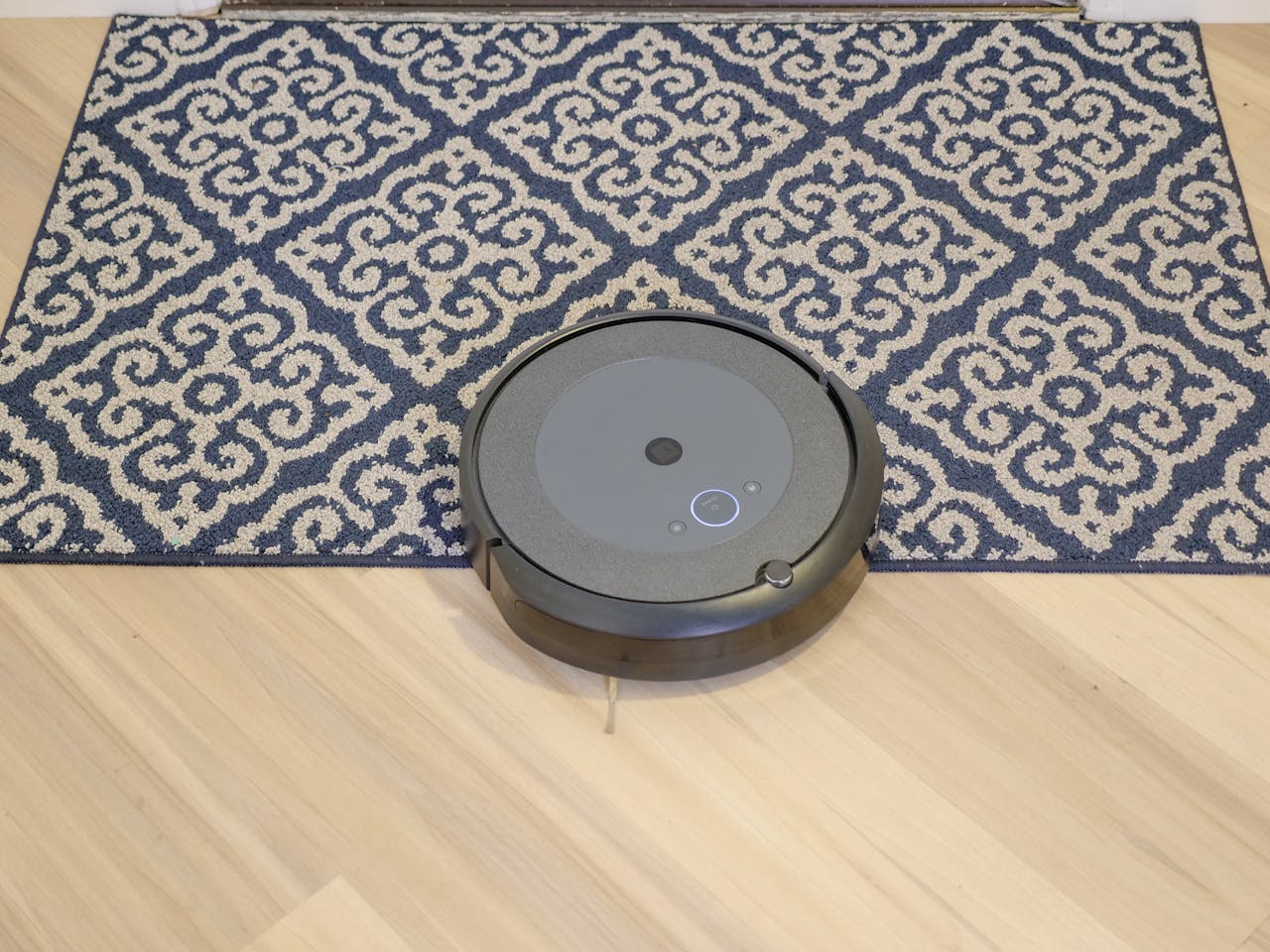 A modern robotic vacuum cleaning a stylish patterned carpet on a wooden floor.